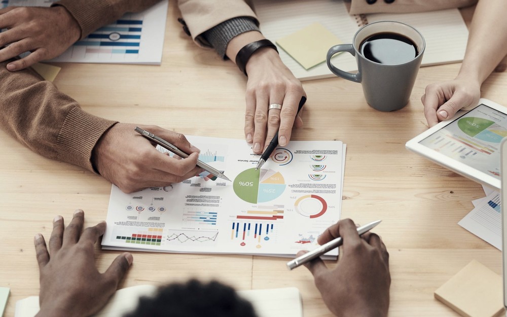 Pessoas analisando gráficos e relatórios em uma mesa de trabalho.