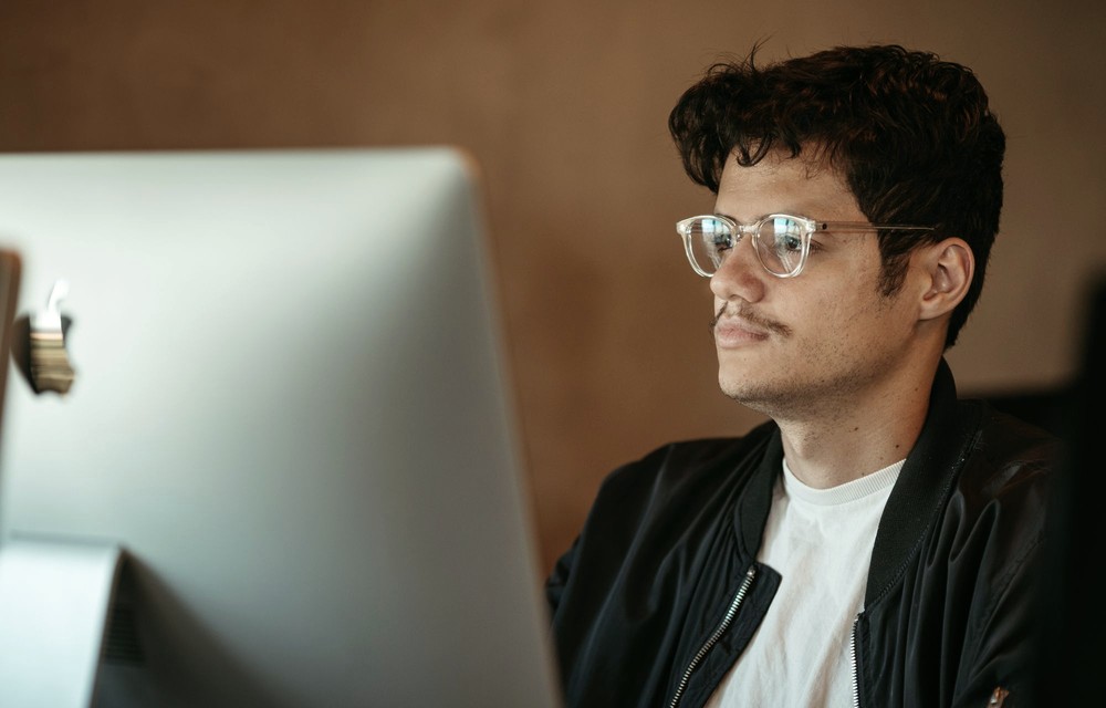 Homem de óculos observando uma tela, com a luz do monitor refletida nas lentes.