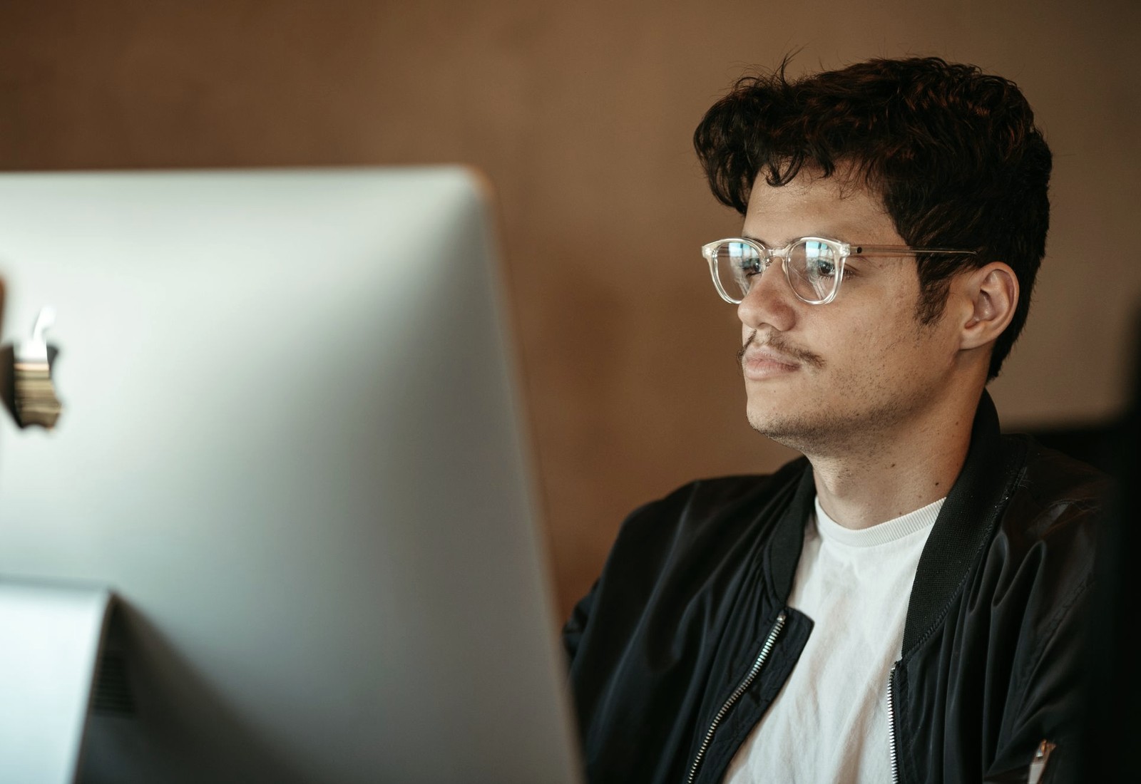 Homem de óculos observando uma tela, com a luz do monitor refletida nas lentes.