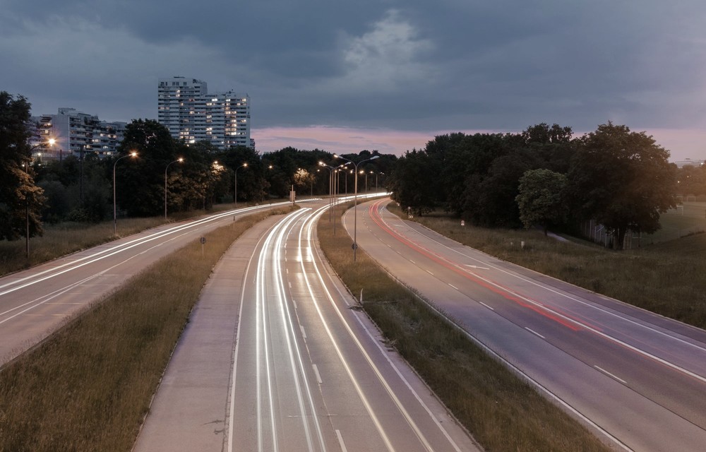 Rastros de luz acompanham uma avenida curva ao anoitecer, registrando o movimento no tempo.
