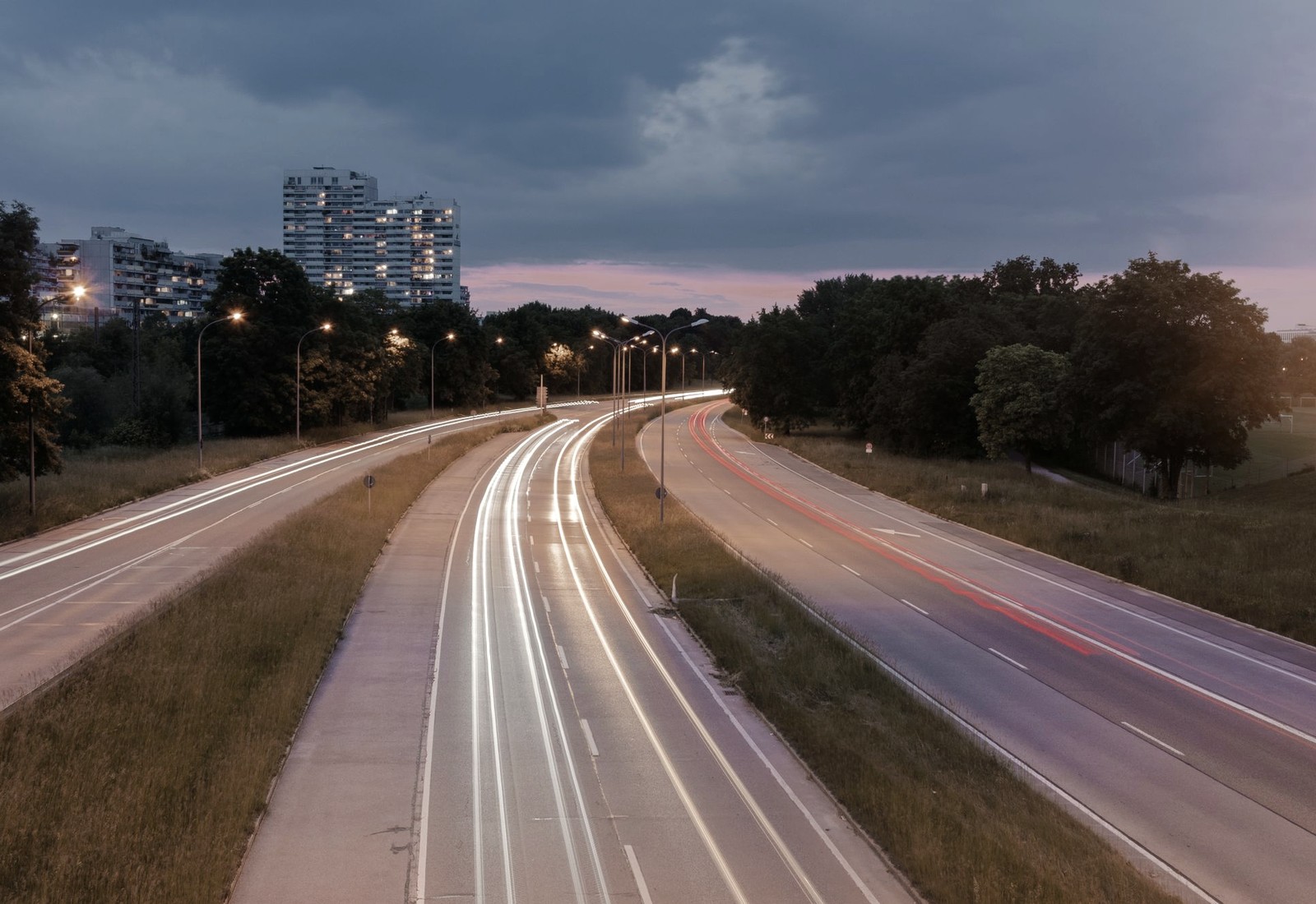 Rastros de luz acompanham uma avenida curva ao anoitecer, registrando o movimento no tempo.